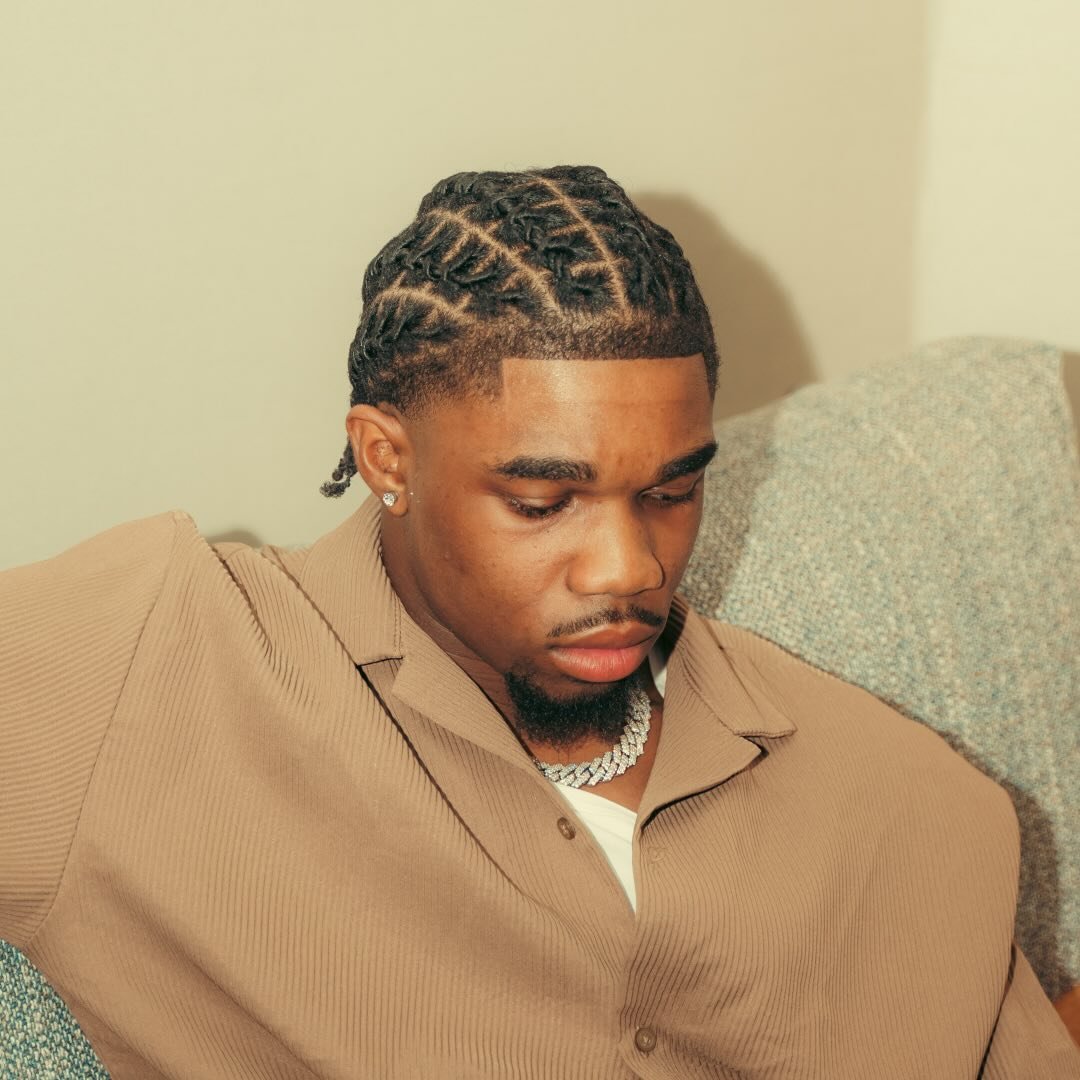Jonathan Ababio wearing a brown shirt with his hair in neat braided twists